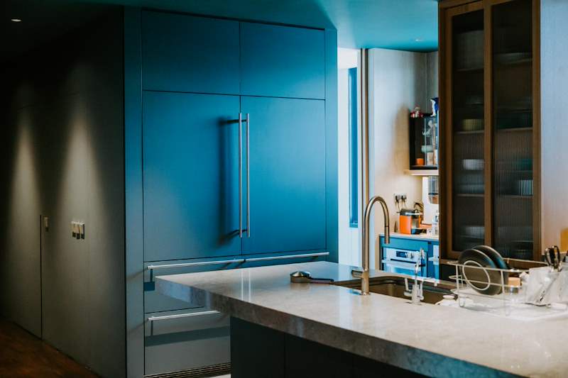 Dark green kitchen cabinets with a stone-topped island and a glass-fronted display cabinet - Condo apartment renovation with a limestone feature wall and dark green kitchen (38MR) | Larry Contractors, HDB Licensed Renovation Contractor, Singapore