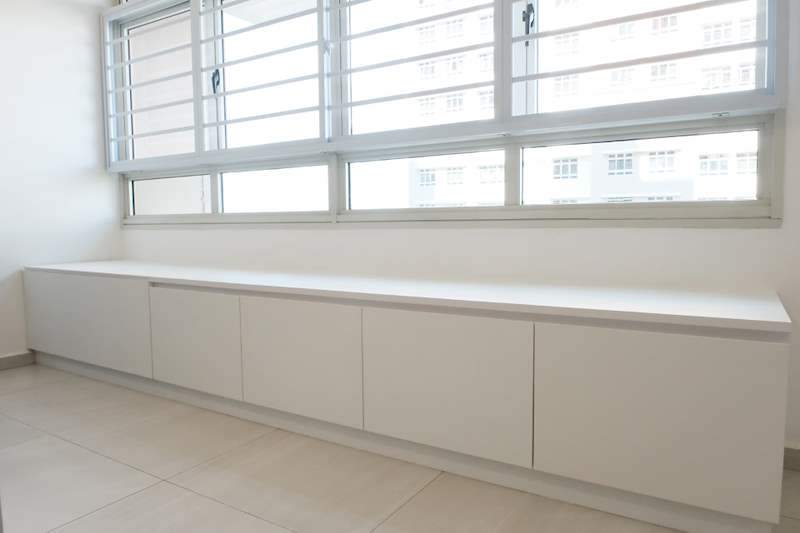 Low white storage cabinets running under the full-width living room windows - HDB flat renovation with a navy kitchen and a glass-walled walk-in wardrobe (407B) | Larry Contractors, HDB Licensed Renovation Contractor, Singapore
