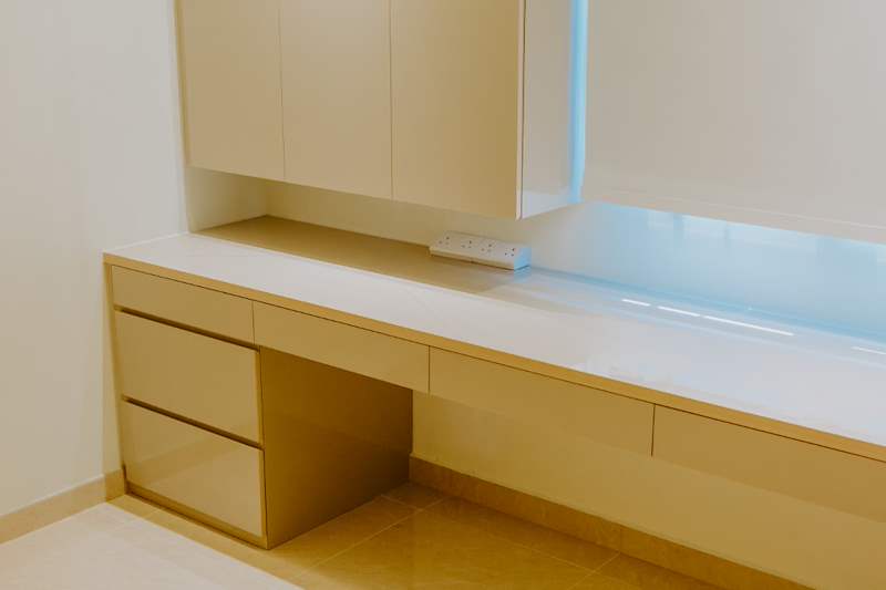 Built-in desk with drawers and overhead cabinets in cream laminate, roller blind behind - HDB flat renovation in cream and mirror-trim laminate with a galley kitchen (C10) | Larry Contractors, HDB Licensed Renovation Contractor, Singapore