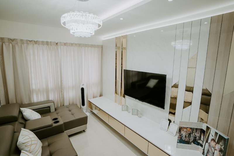 Living room TV wall in cream laminate with mirror strips, tiered crystal light and sheer curtains - HDB flat renovation in cream and mirror-trim laminate with a galley kitchen (C10) | Larry Contractors, HDB Licensed Renovation Contractor, Singapore