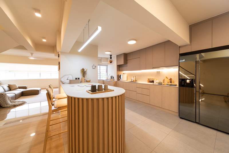 After: beige kitchen with a curved timber-slat island, a stainless fridge and under-cabinet lighting - Full HDB maisonette renovation with a curved timber-slat island and lit staircase (140BB) | Larry Contractors, HDB Licensed Renovation Contractor, Singapore