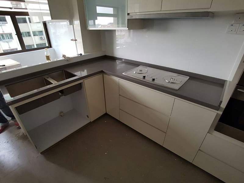 During installation: the grey worktop with the hob and sink openings cut, cabinet carcasses below and windows above - HDB kitchen carpentry in cream laminate with a built-in oven (C07) | Larry Contractors, HDB Licensed Renovation Contractor, Singapore