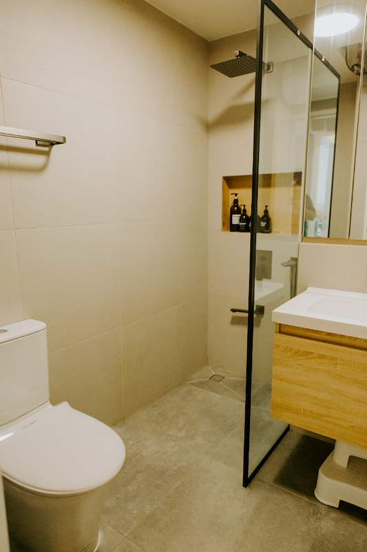 Bathroom with a glass shower screen, oak vanity and wall-hung toilet - Full HDB maisonette renovation with a curved timber-slat island and lit staircase (140BB) | Larry Contractors, HDB Licensed Renovation Contractor, Singapore