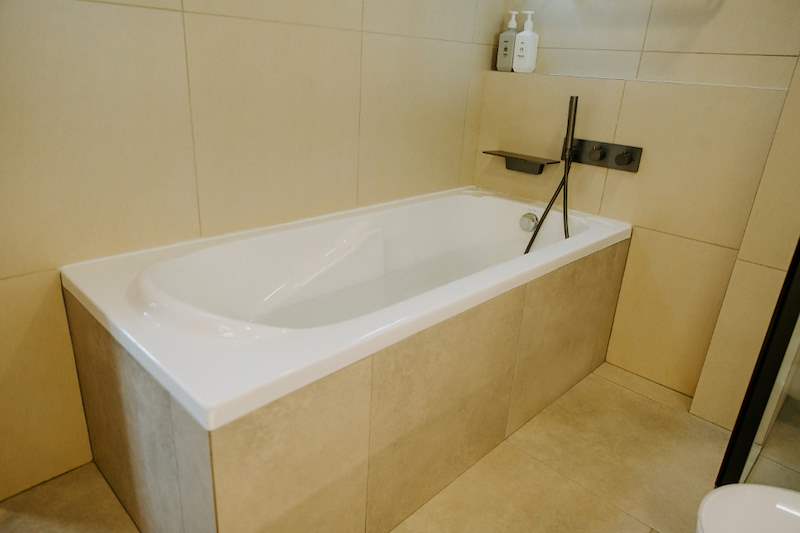 Built-in bathtub with a stone-look surround and a wall-mounted black tap - Full HDB maisonette renovation with a curved timber-slat island and lit staircase (140BB) | Larry Contractors, HDB Licensed Renovation Contractor, Singapore
