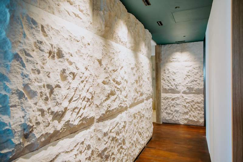 Rough-cut limestone feature wall lit from above, with dark timber flooring - Condo apartment renovation with a limestone feature wall and dark green kitchen (38MR) | Larry Contractors, HDB Licensed Renovation Contractor, Singapore